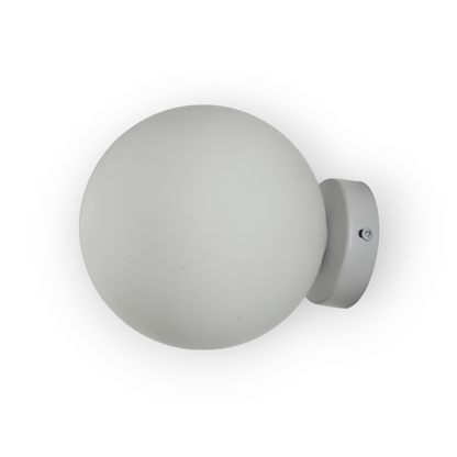 The image displays the Elio Wall Light, a minimalist fixture featuring a base and a frosted glass globe that diffuses light evenly, creating a soft and welcoming ambiance suitable for various interior settings.