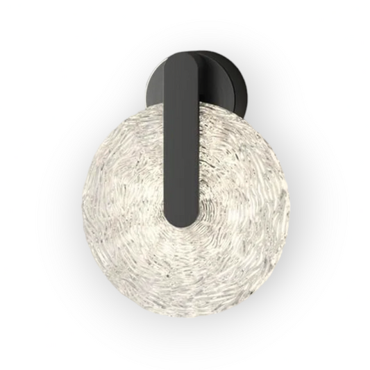 The image captures the Maris Wall Light, which features a striking spherical shade with an intricate textured pattern, anchored by a sleek, matte black arm. This juxtaposition of organic form and modern design creates a captivating visual interest.