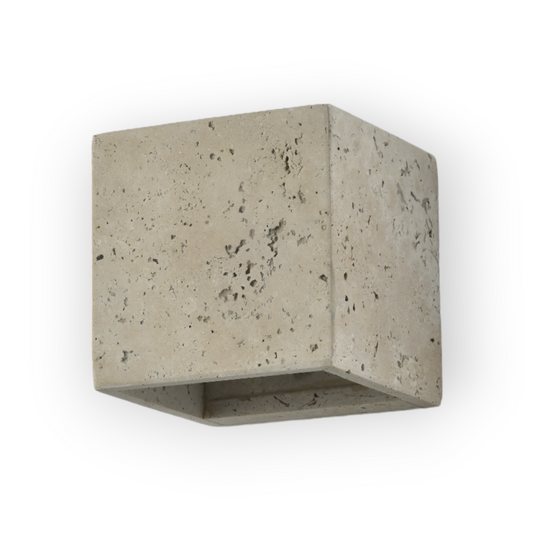 This image exhibits the Nova Wall Light, a cubed fixture crafted from travertine stone, providing a soft glow that highlights the natural pores and patterns of the material, lending a raw yet refined look to any space.